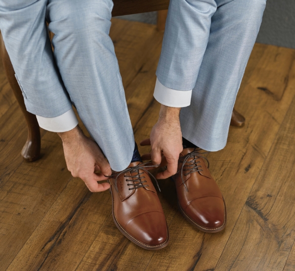 Shop Stacy Adams Wedding Picks. Image features a man tying the Maddox cap toe oxford in cognac.