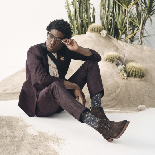 "Shoe Style Quiz: Choosing Shoes That Match Your Personality." The featured image is a model sitting by the sand in the Kyron Plain Toe Lace Boot in Brown Multi.