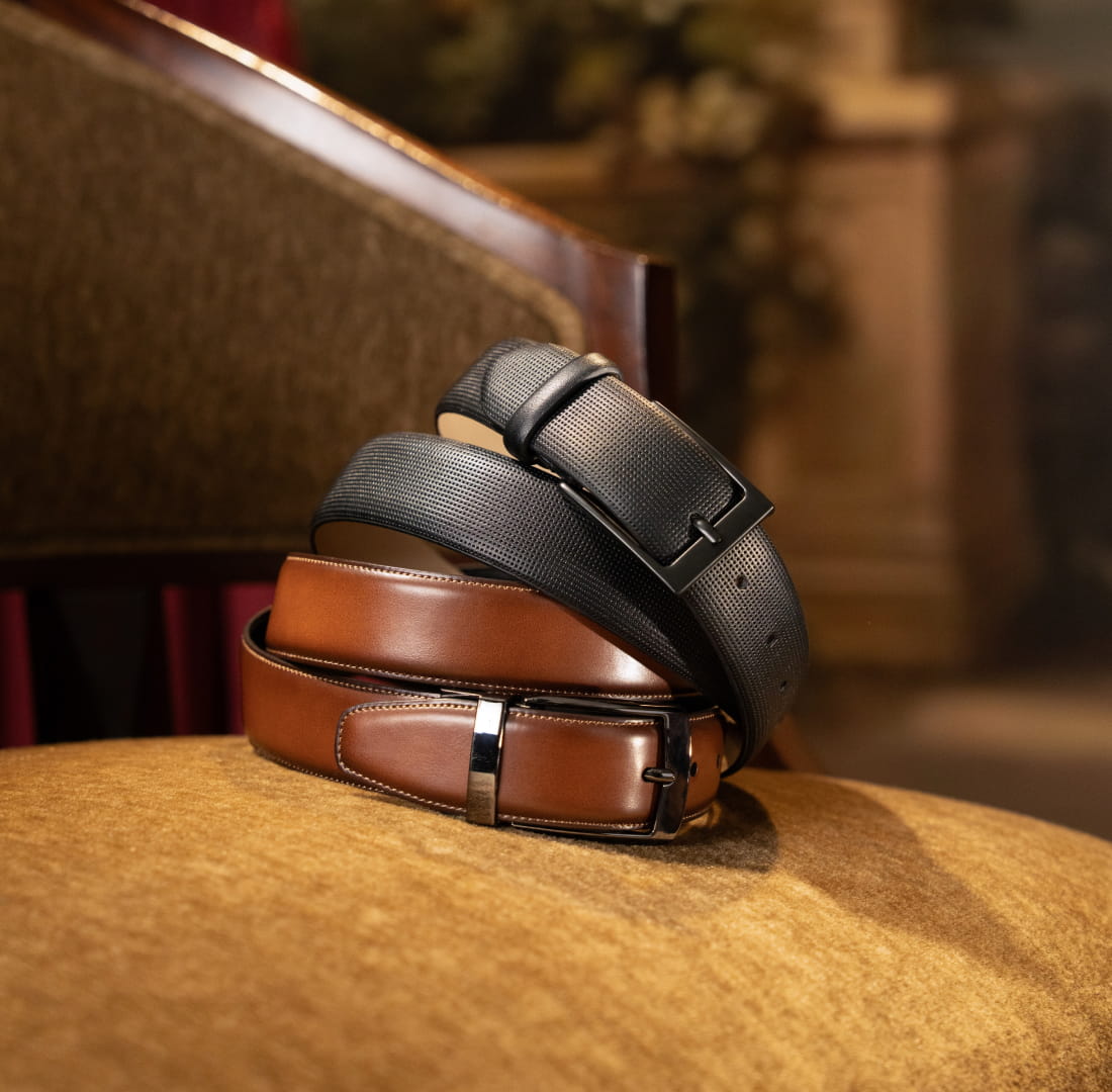 Shop Stacy Adams belts featuring 2 styles on a suede chair.