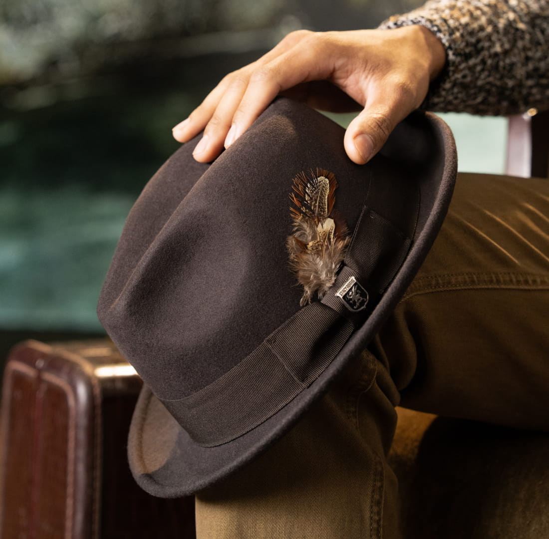 Shop Stacy Adams Hats featuring the August Fedora in Brown on a man's knee with a suitcase in the background.