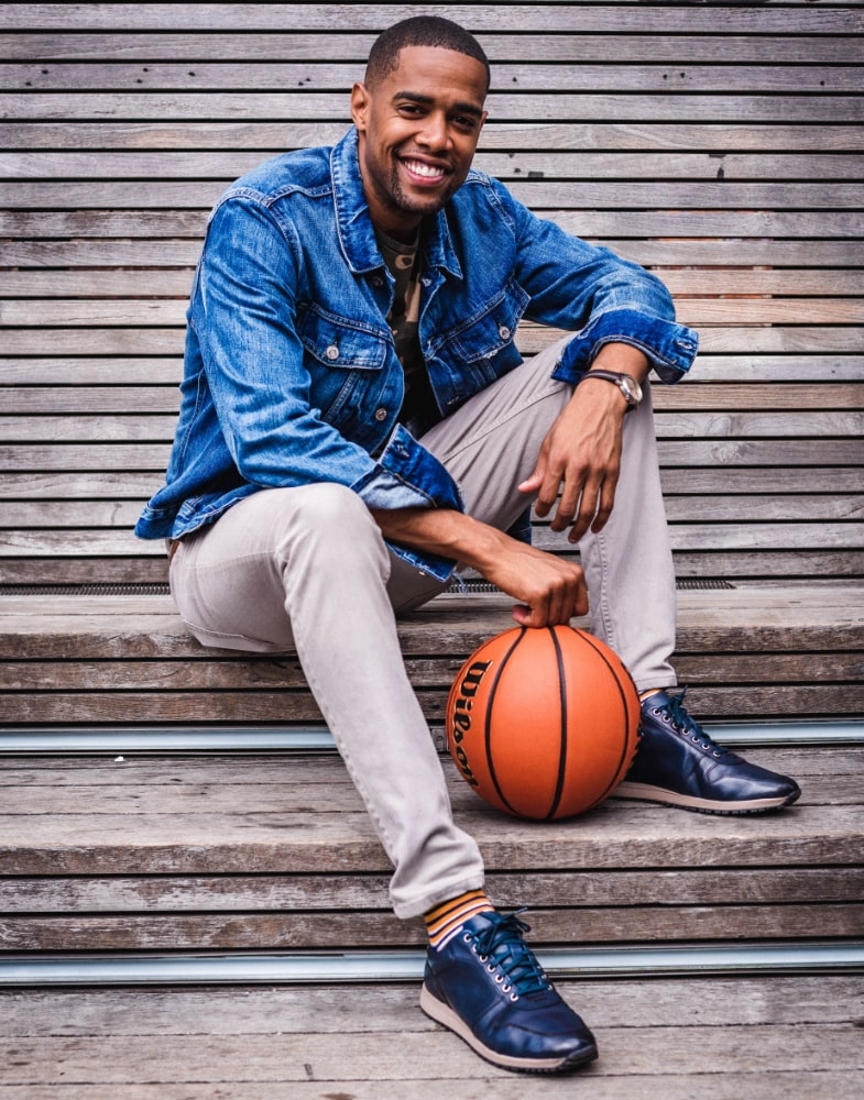Image of social media influencer and Harlem Globetrotter Brawley Chisholm wearing the Axel Moc Toe Lace Up in Navy while sitting on the steps with a basketball.
