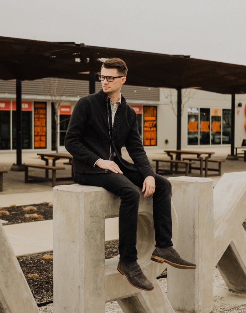 Image of social media influencer Matt Hartman wearing the Colfax Moc Toe Penny Slip On in Gray Suede while sitting on a sign.