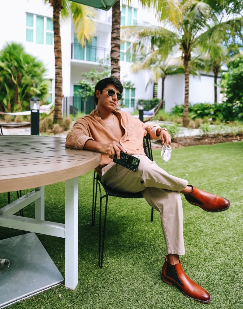Image of social media influencer Marco Arrieta sitting at a table outside wearing the Fabian Plain Toe Chelsea Boot in Cognac.