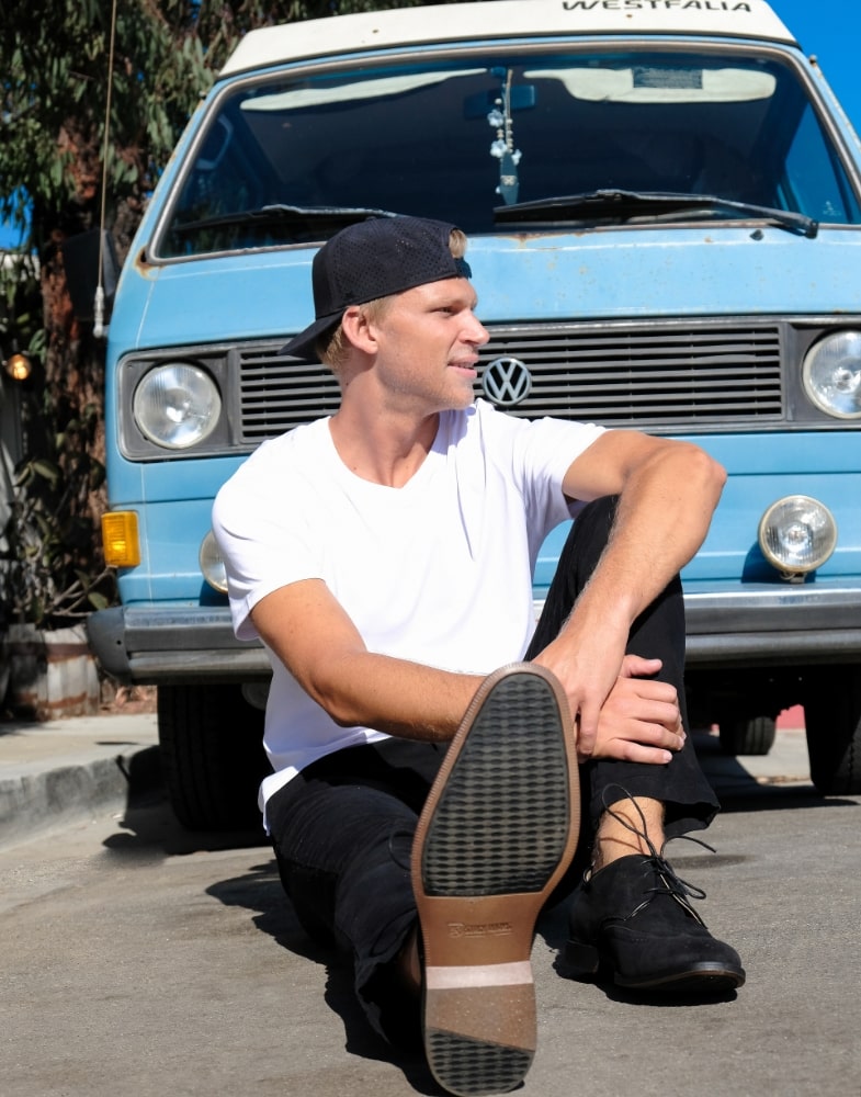 Image of social media influencer Drew Mellon wearing the Wickersham Wingtip Oxford in Black Suede while casually sitting on the ground.