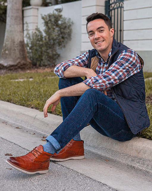 Image of social media influencer Alessandro Pontes sitting outside wearing the Sentinel Plain Toe Boot in Cognac.
