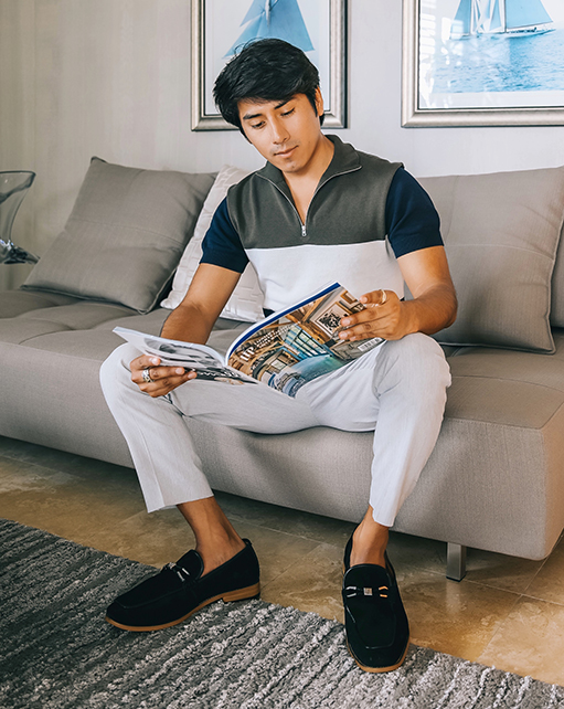 Image of social media influencer Marco Arrieta inside reading a magazine while wearing the Colbin Moc Toe Ornament Strap Slip On in Black Suede.