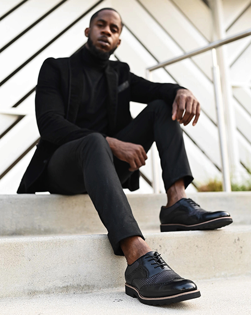 Image of social media influencer Chidi Ezemma sitting on steps while wearing the Callan Wingtip Oxford in Black.
