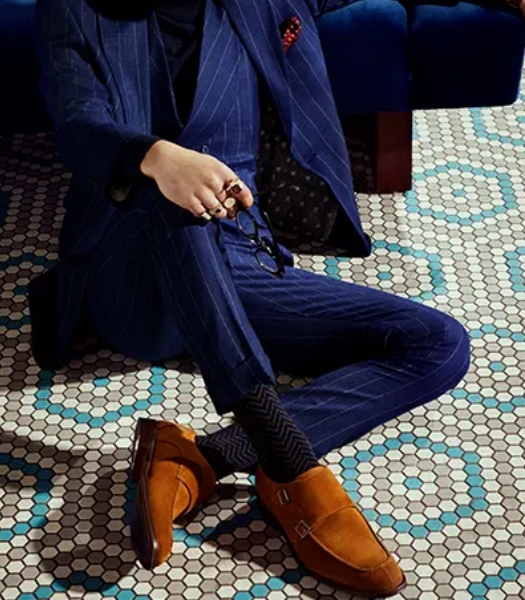 The featured image is a model leaning on a bench in a blue pin-stripped suit and tan monk strap shoes.