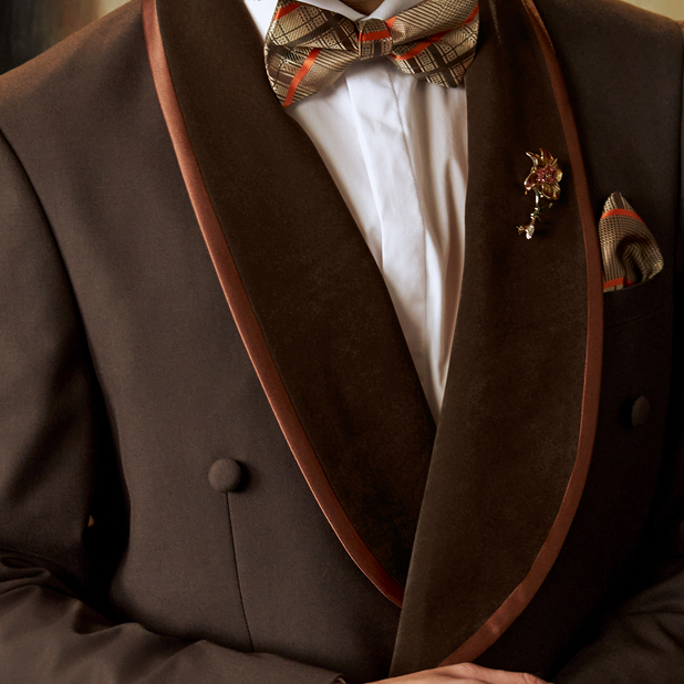 "When Wearing A Tuxedo, Make Sure Your Black Tie Attire Shines." The featured image is of a model wearing a brown suit jacket with orange trim, a white dress shirt, and a plaid orange and brown bow tie with a matching pocket square.