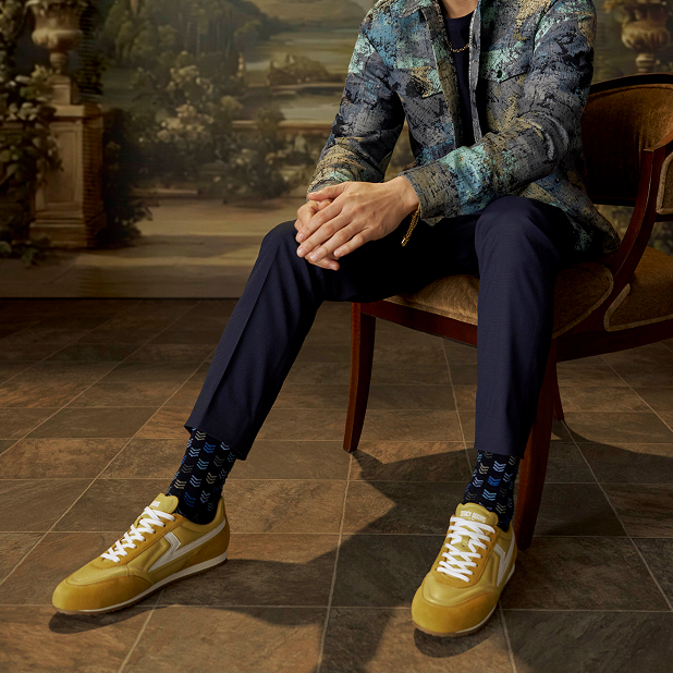 "Finding Men's Fashion Advice Using Social Media." The featured image is of a model wearing a colorful dress shirt, dark blue pants, patterned socks, and the yellow Action 150s while sitting on a wooden velvet chair. 