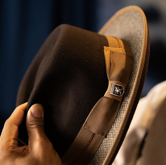 "Follow These Men's Style Tips For A Stylish Look From Head To Toe." The featured image is of the Zylen Fedora Wool Felt Pinch Front Hat in brown, being held by a model against a dark blue background.