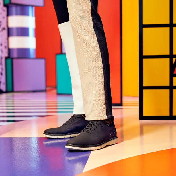 "Fashion For Men: How To Make A Statement With Your Outfit." The featured image is a model wearing black lace-up shoes in a room with multi-colored geometric patterns.