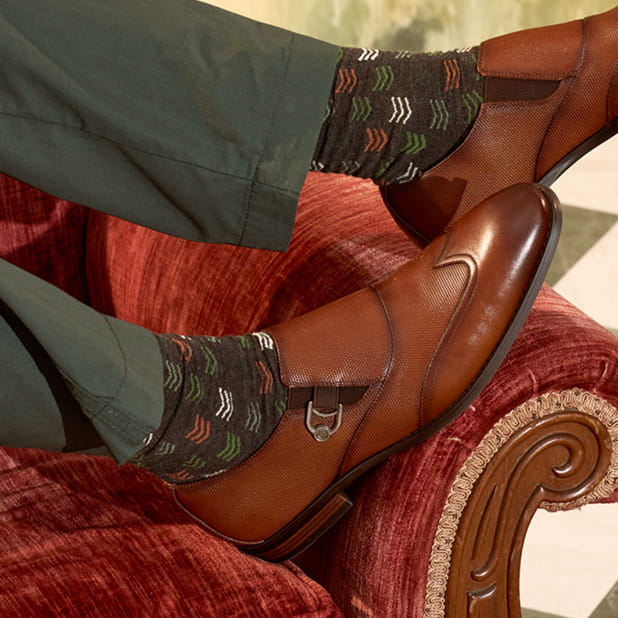 "Finding Men's Fashion Advice Using Social Media." The featured image is a close-up of a model wearing Stacy Adams patterned socks and the Lockwood Wingtip Ornament Slip Ons in Cognac on a red couch. 
