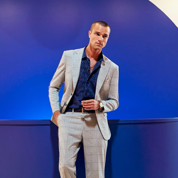 "What To Wear For A Wedding: Outfits For Men." The featured image shows a man dressed in a light grey suit and a dark blue button-up on a blue background.