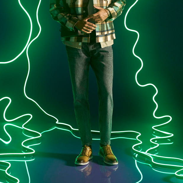 "Work From Home in Style" The featured image shows a model wearing the Stacy Adams Sync Plain Toe Elastic Lace Ups in the color Natural surrounded by winding neon lights on a purple background.